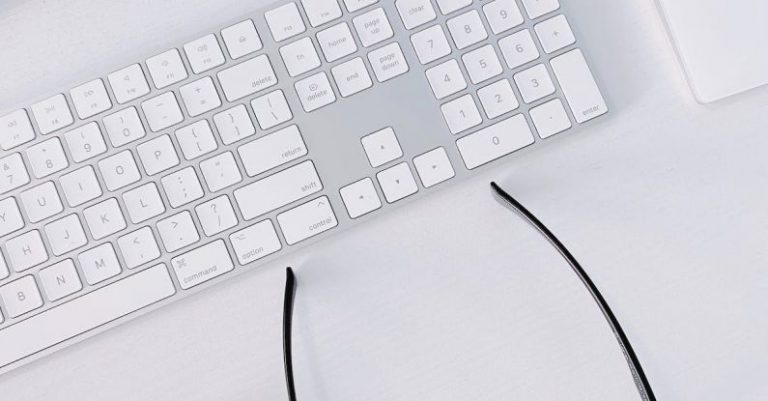 Peripherals - Wireless Keyboard and Airpods Case Next to Glasses