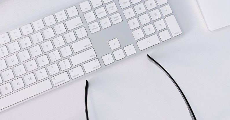 Peripherals - Wireless Keyboard and Airpods Case Next to Glasses